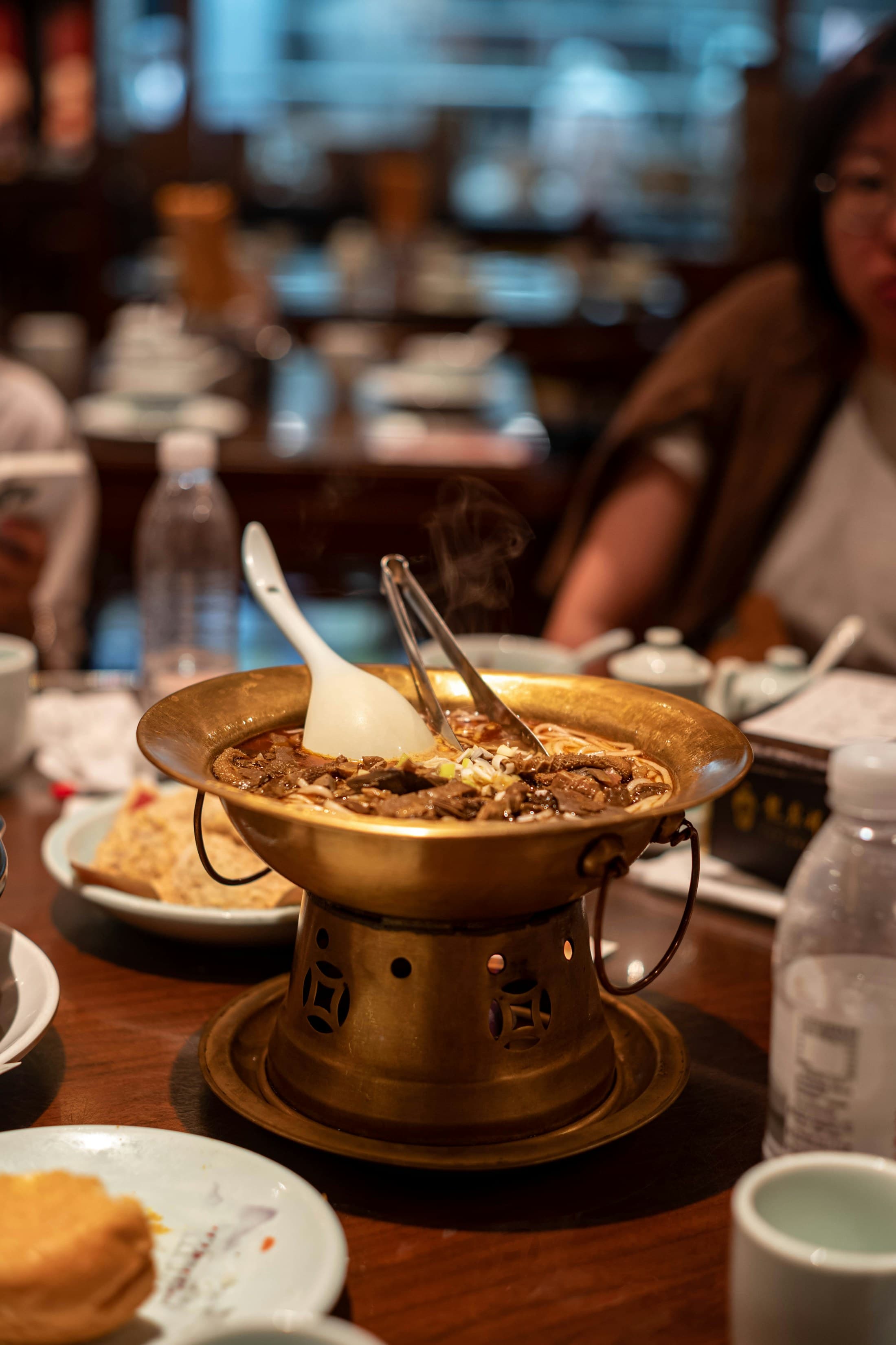 A steaming brass hot pot on a busy restaurant table